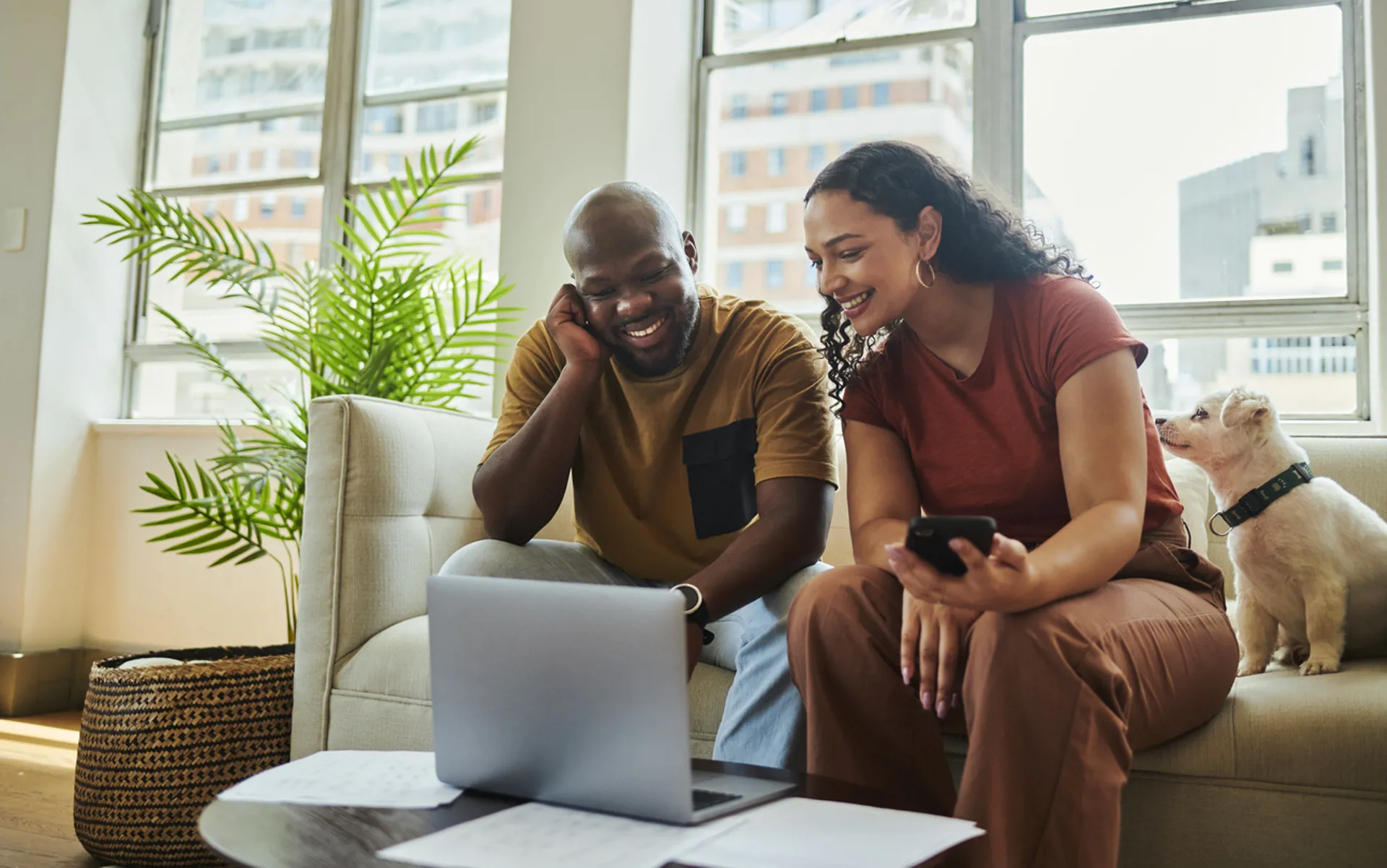 A young couple sitting on the couch working on their finances with a laptop computer looking at each other while smiling
