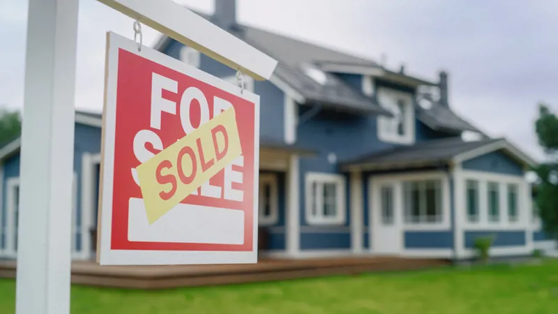 Close Up of a House Sold Sign on a Lawn in Front of a Big Modern House with Traditional Architecture