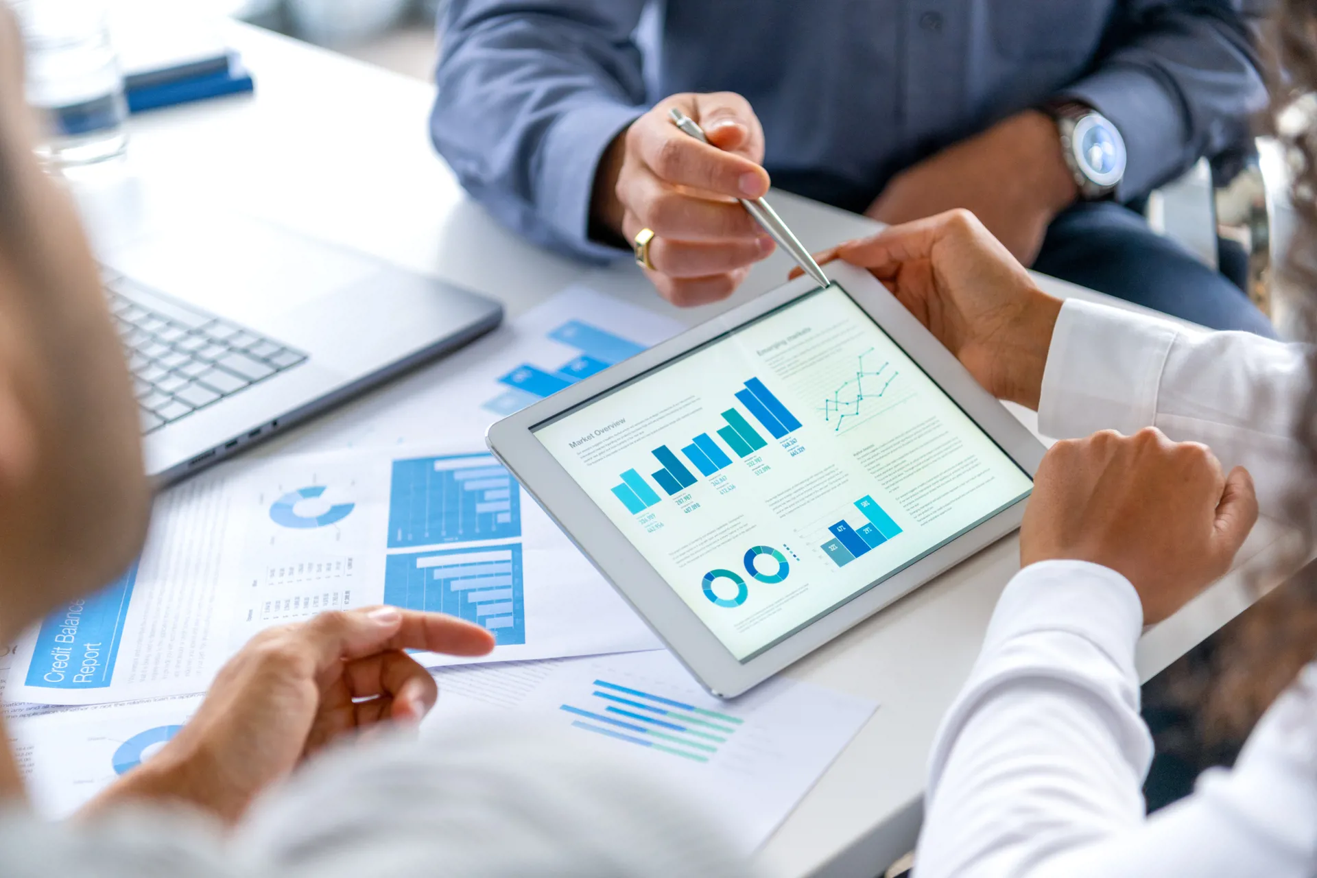 Close up of three people looking at financial data with graphs and charts