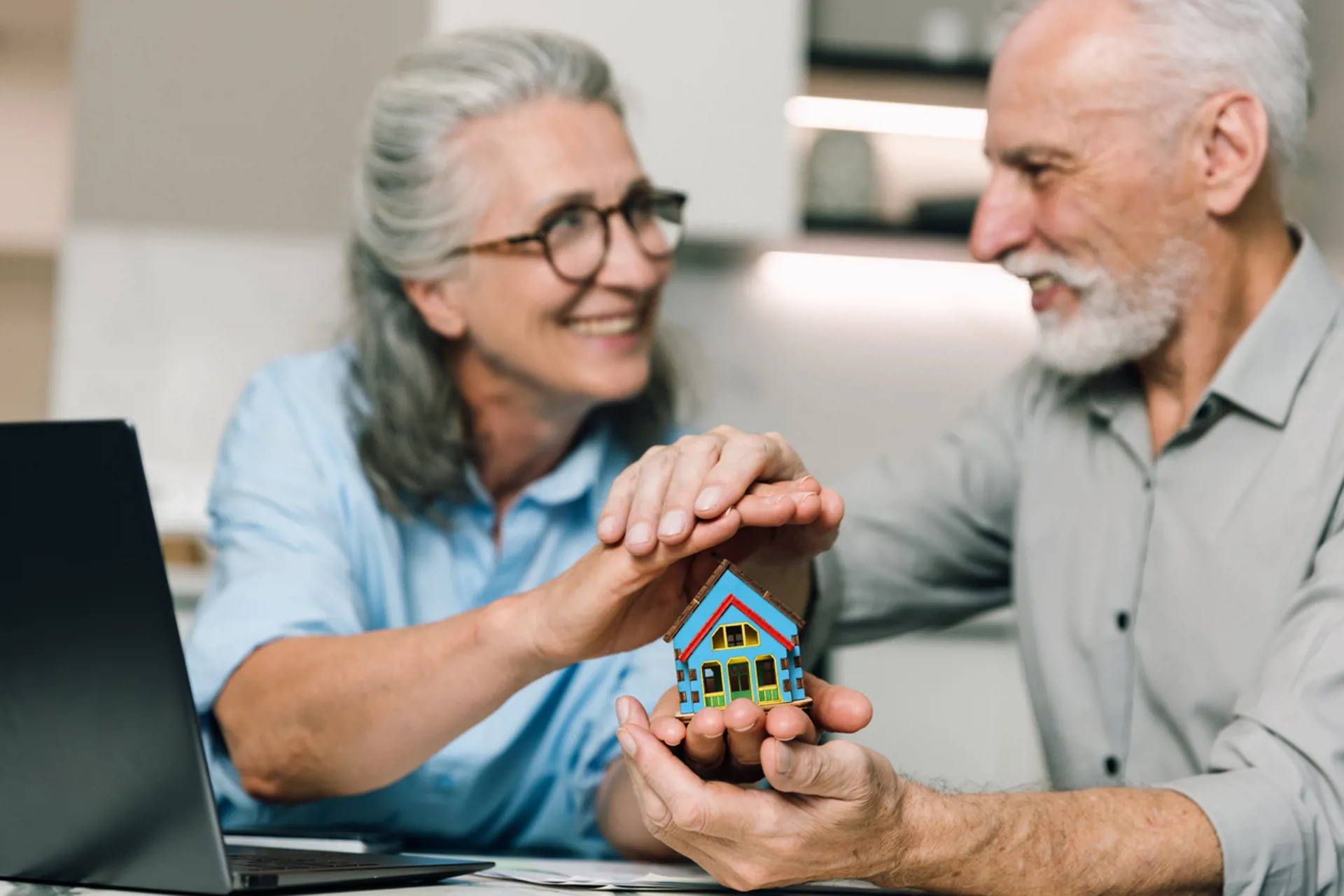 Elderly couple discusses home finances while using a laptop at their kitchen table