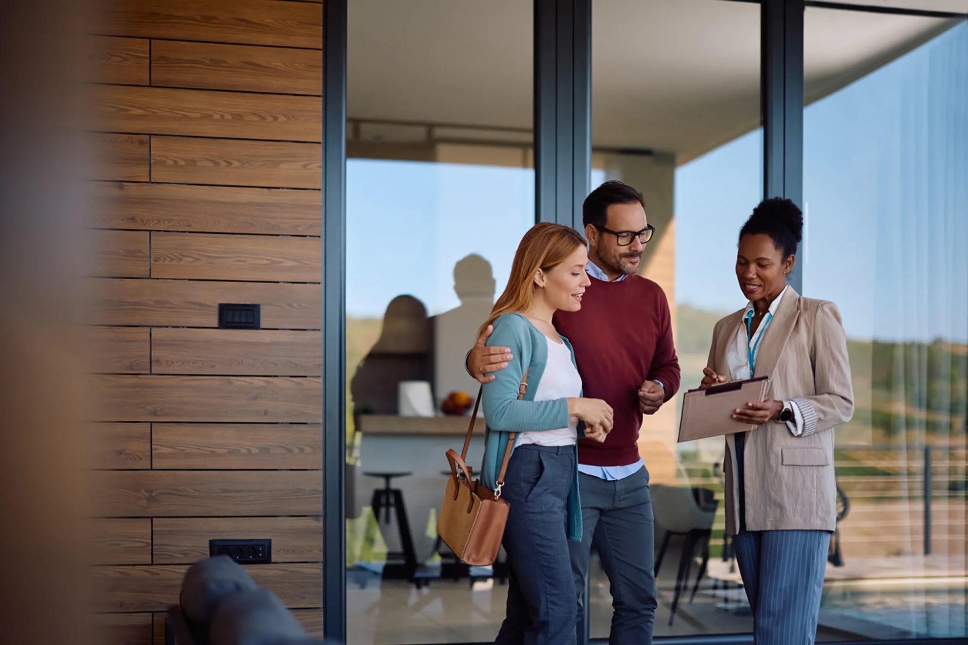 Smiling couple and their real estate agent analyzing paperwork during open house day