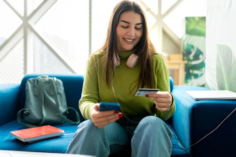Woman sitting on couch holding card and cellphone