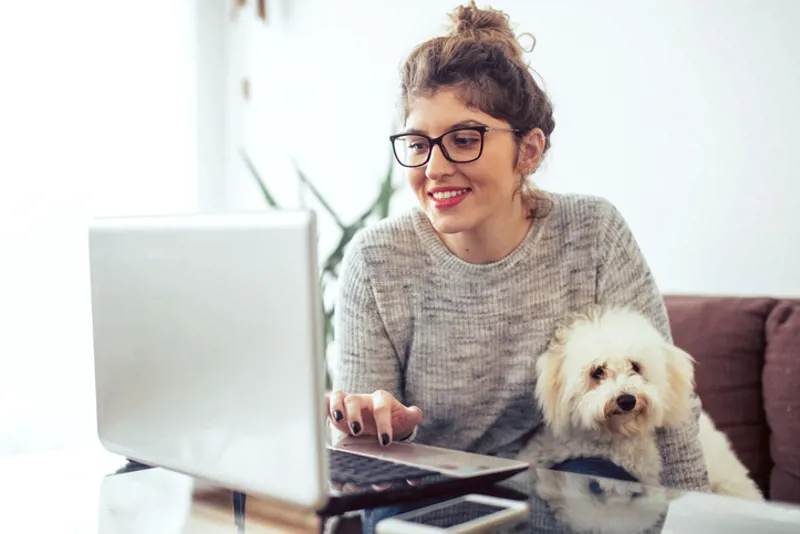 Young woman holding a dog working at her home