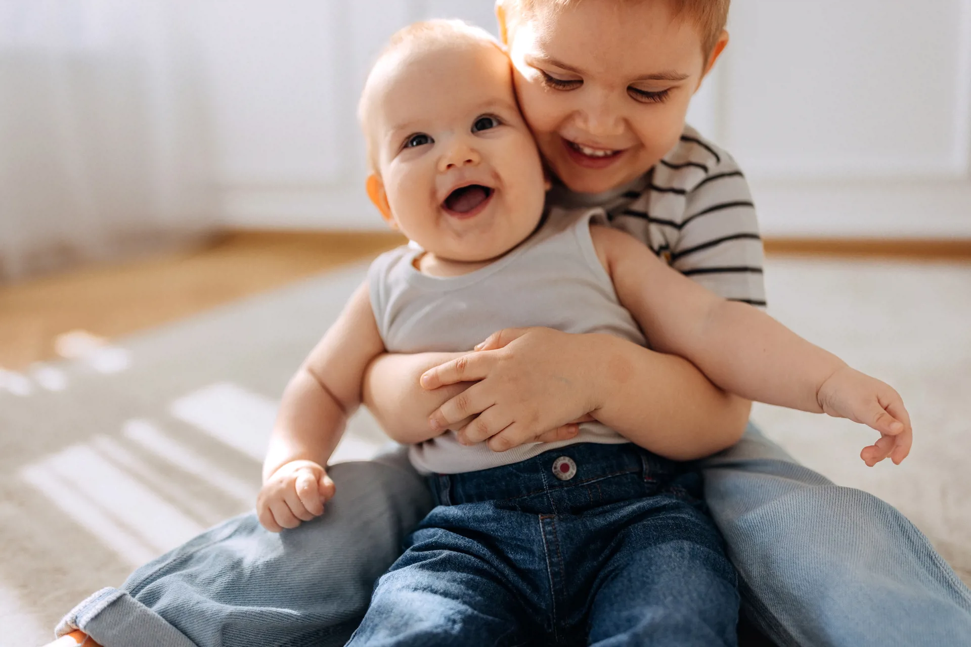 Two young children smiling and hugging on the floor.