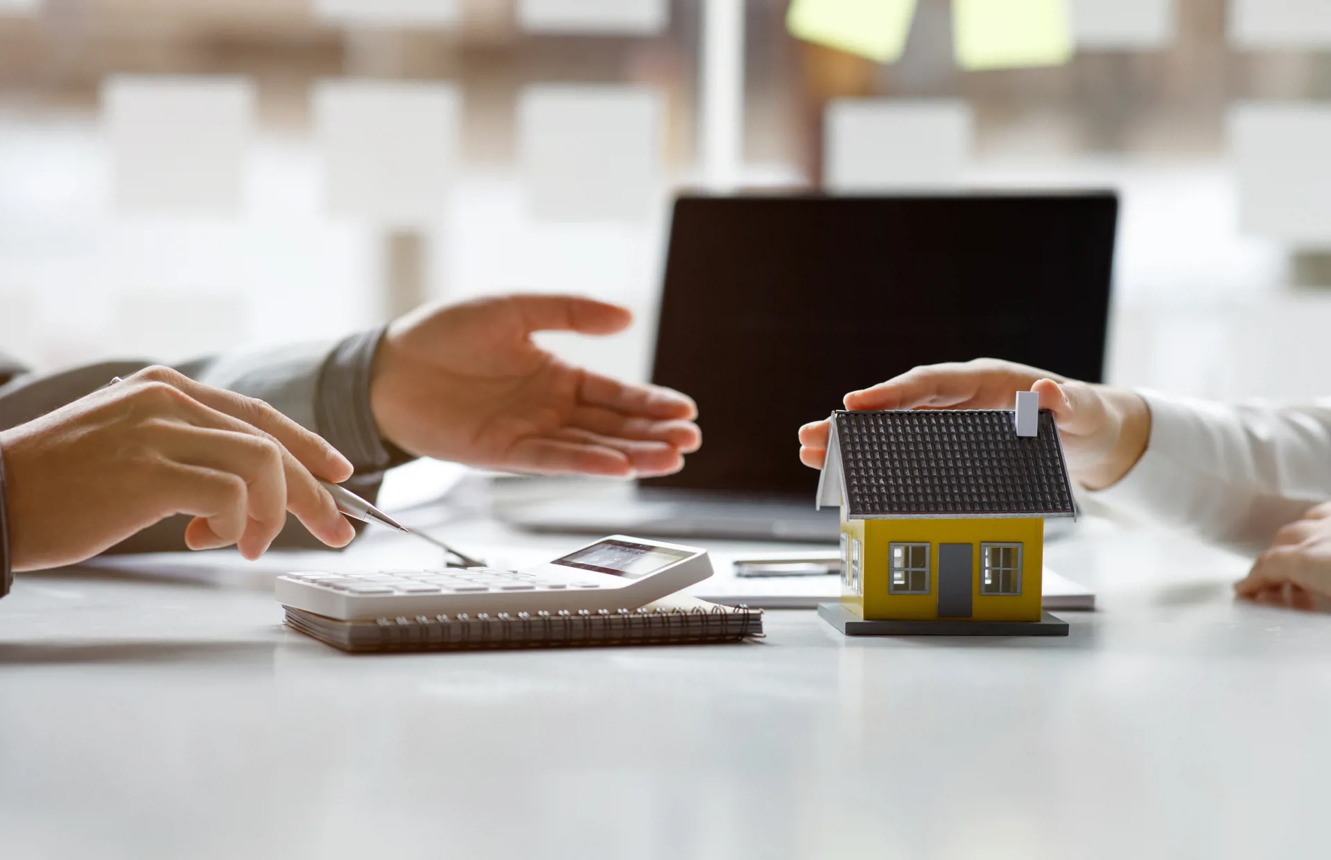 Hands above desk with small house ornament